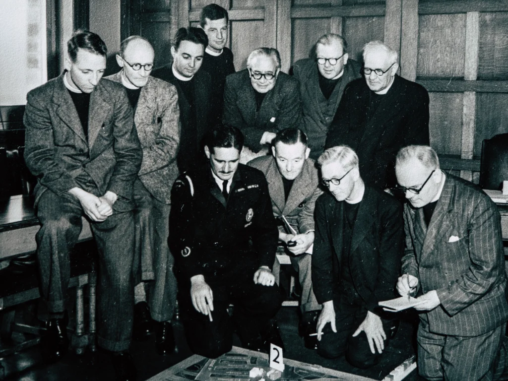 A vintage photograph showing a group of men huddled around a map, in 1951